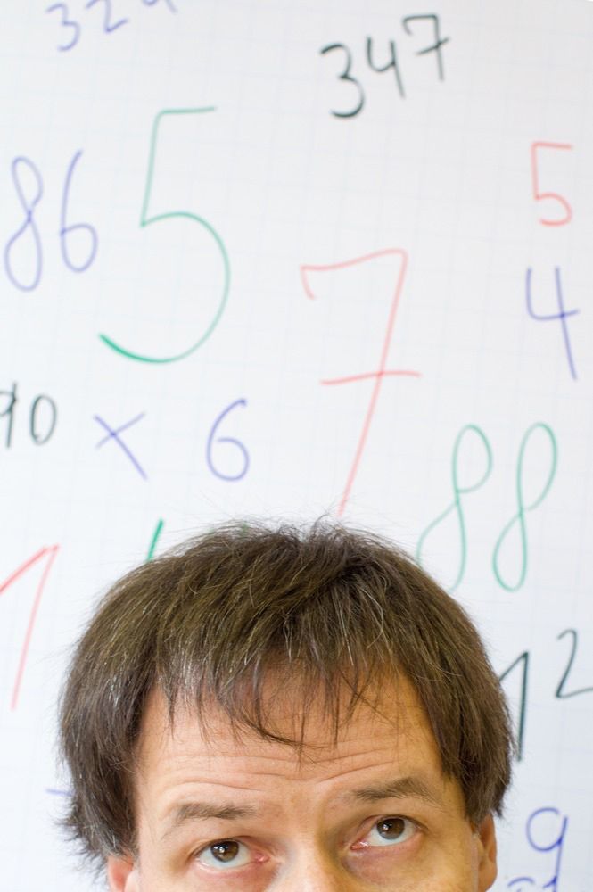 Toppen av et hode foran en vegg med tall. Foto.