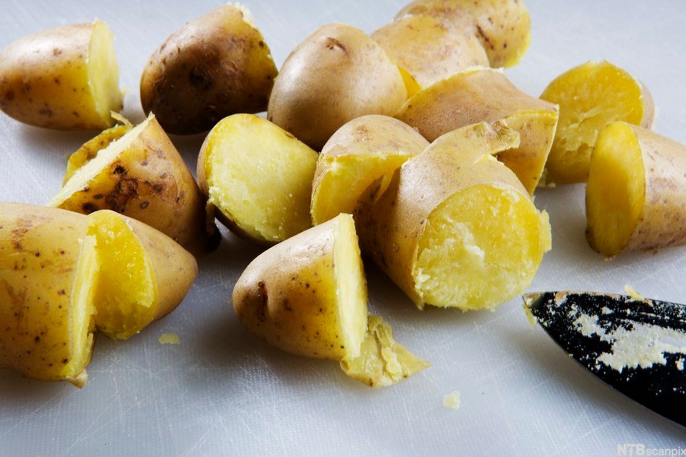 Flere kokte mandelpoteter med skall, delt i biter på ei skjærefjøl. Foto.