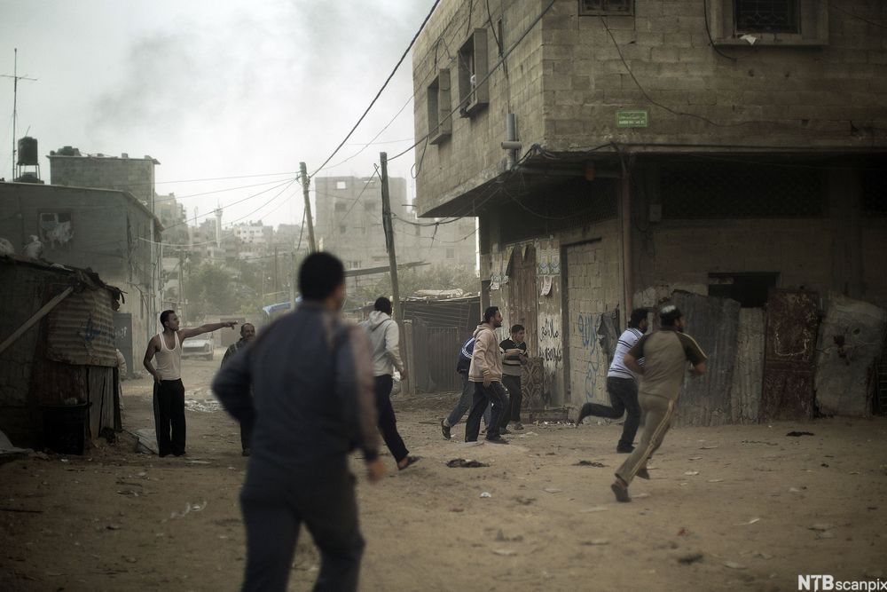 Unge menn flyktar gjennom gater prega av øydeleggingar. Foto.