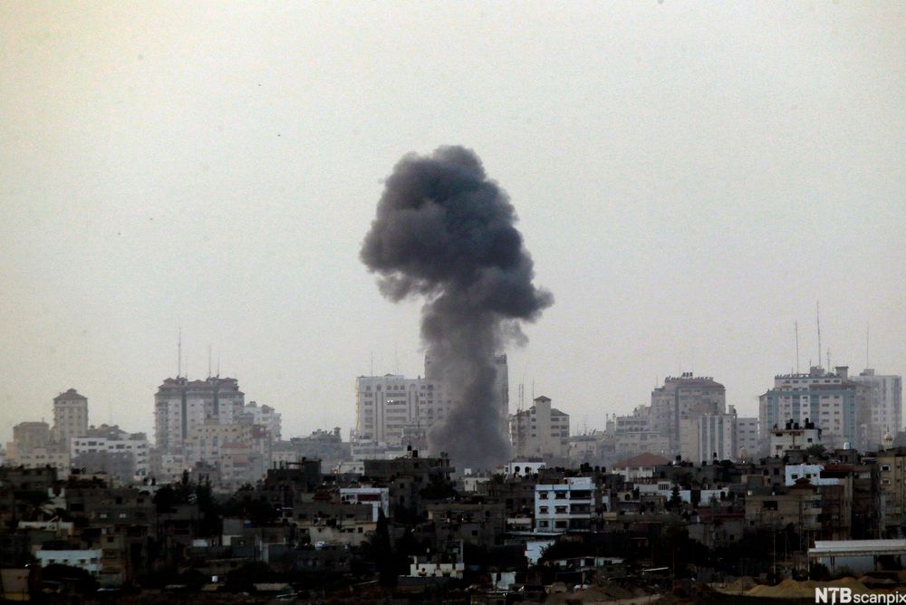 Svart røyk stig opp midt i ein by. Foto.