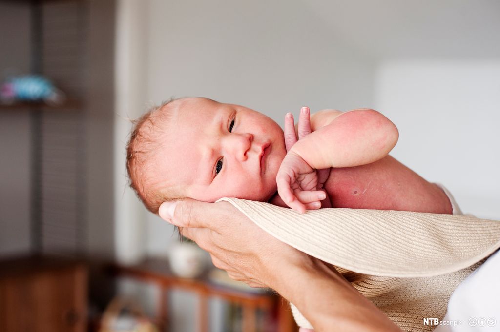 Naken baby blir holdt. Foto.