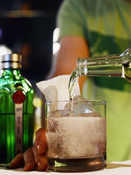 Ein mann heller tonicvatn i eit drinkglas. Ved sida av står ei flaske med gin. Foto.