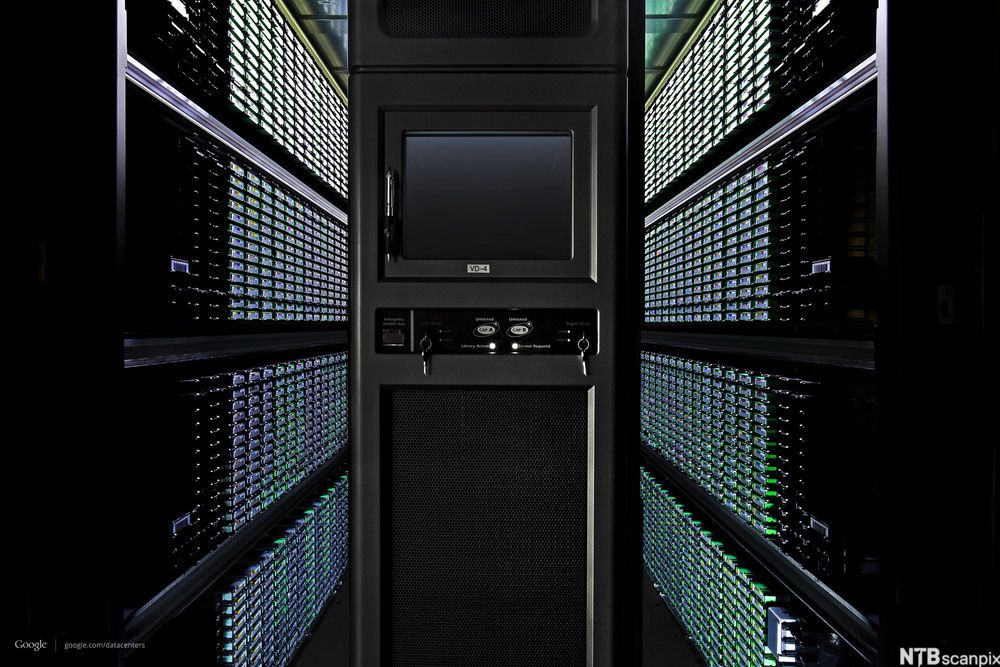 Foto frå eit av Googles datasenter. Biletet viser eit mørkt rom tettpakka med lagringseiningar frå golv til tak. Det lyser i grøne lamper frå mange av datadiskane.