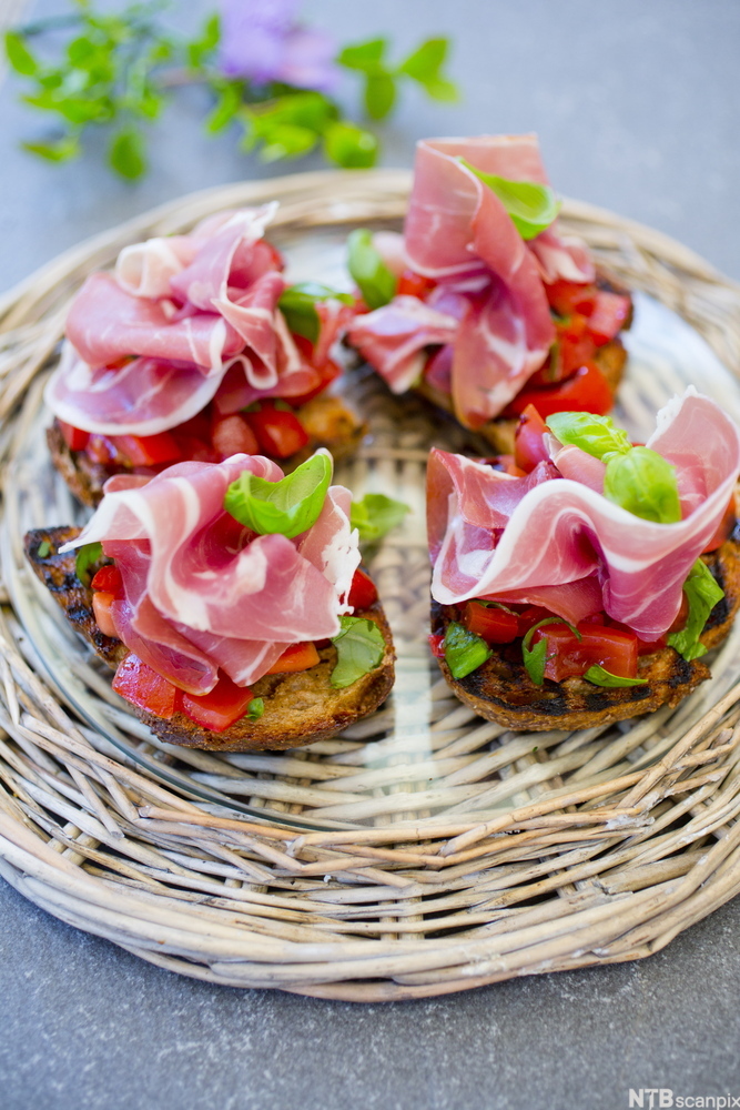 Fire fargerike bruschetta serverte på eit rundt rottingfat. Foto.