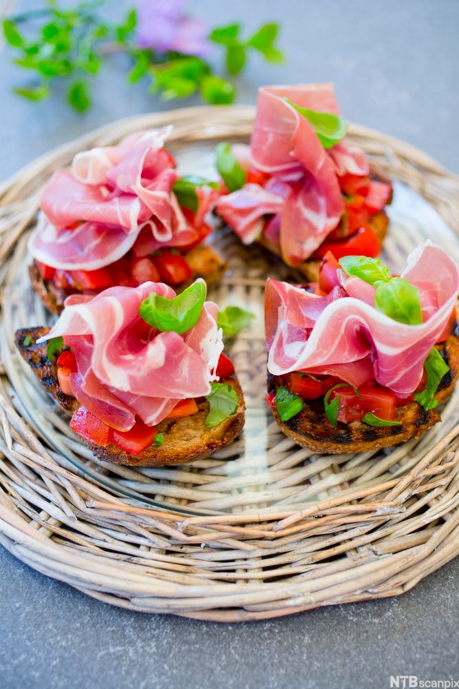 Fire fargerike bruschetta servert på et rundt rottingfat. Foto.