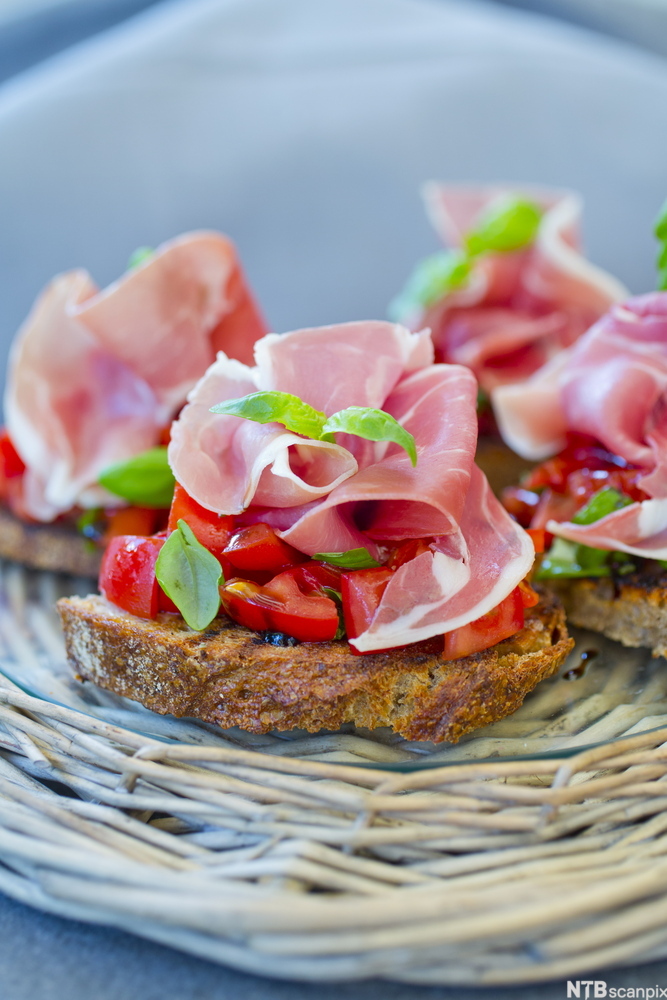 Brødskiver med spekeskinke, tomat og grønne urter. Foto.