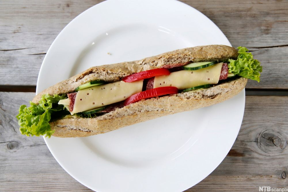 Ein grov bagett med salat, ost, salami, paprika og tomat. Foto.