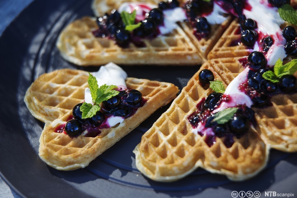 Vaffelhjarte på ein tallerken. Vaflane er laga med solbær, rømme og eit grønt blad som garnityr. Foto.