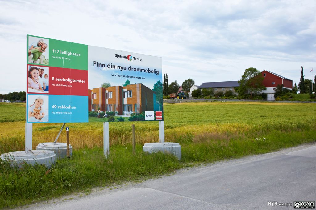 Reklameskilt langs veien, som står tett innpå dyrka mark. Foto.