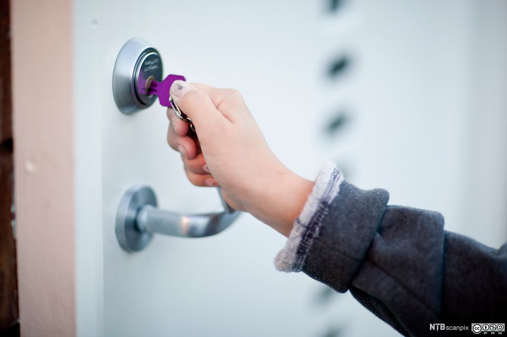 Nærbilde av ei hånd som låser opp ei dør. Foto.