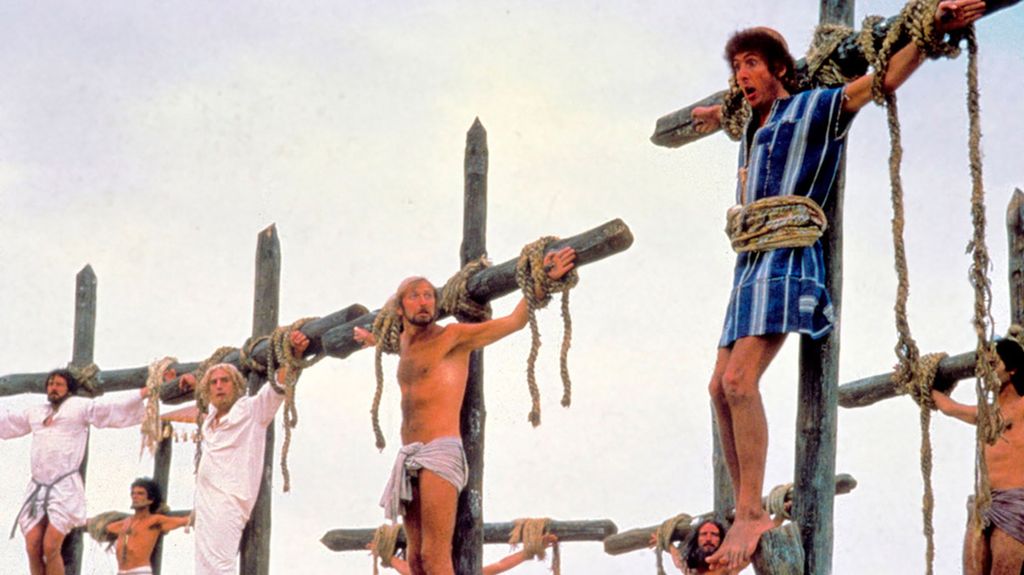 Framstilling fra filmen *Life of Brian*. Flere menn henger på hvert sitt kors. Hovedpersonen Brian har en blåstripete kjortel på seg og har åpen, måpende munn. Foto.