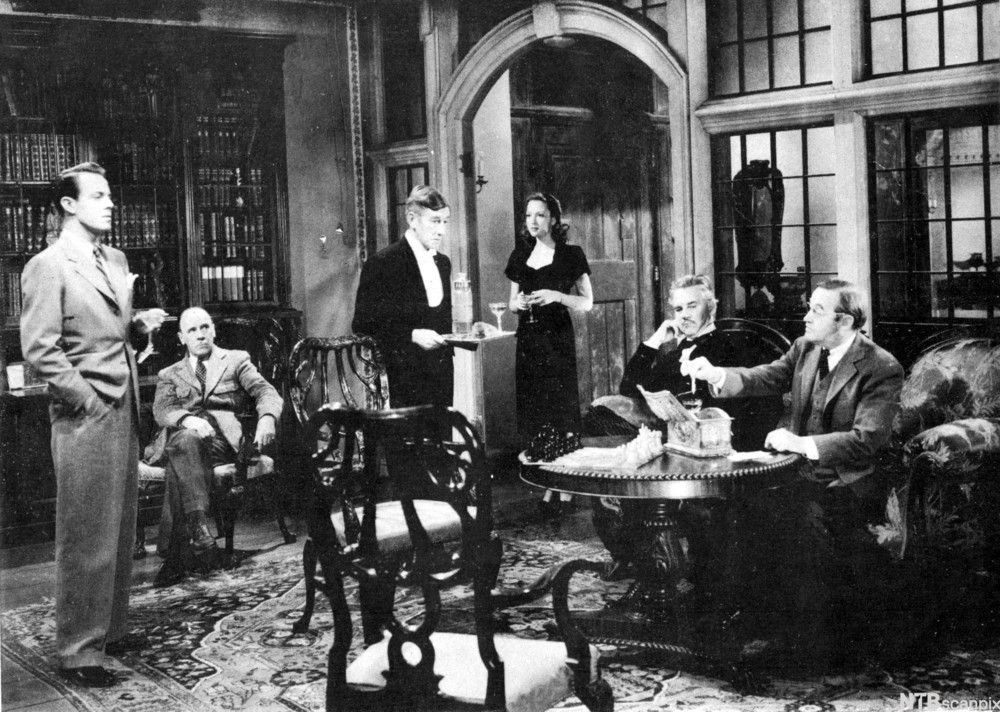 Filmscene fra bibliotek der de mistenkte i en krimgåte er samlet. Foto.