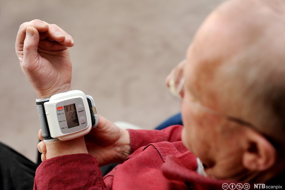 Eldre mann med blodtrykksmåler rundt håndleddet. Foto.