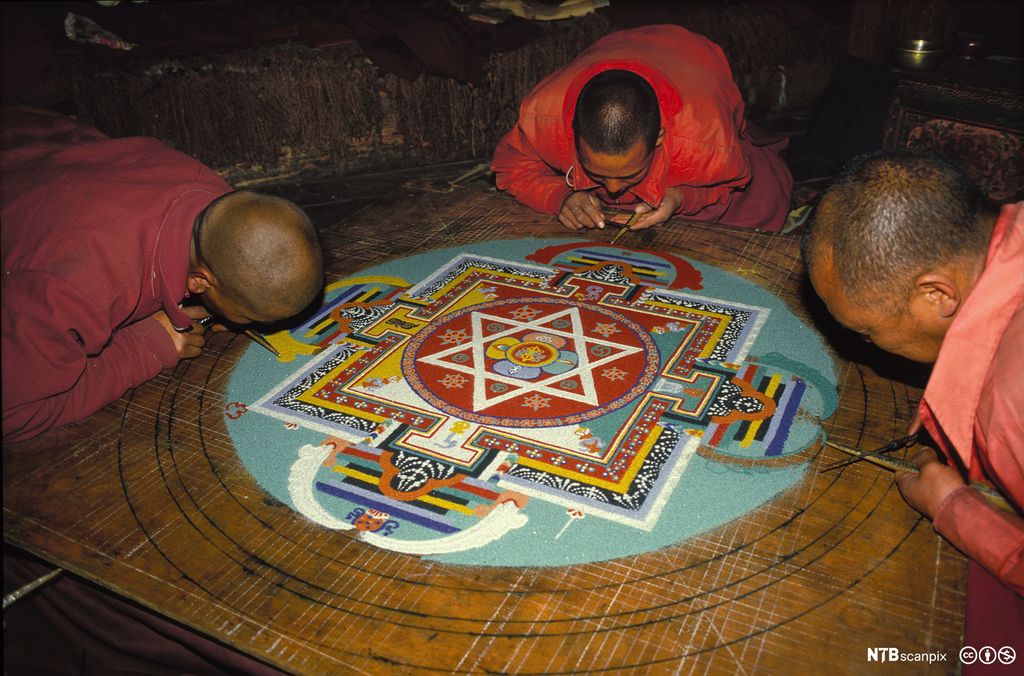 Tre munker lager kunstverk av sand i ulike farger. Foto.