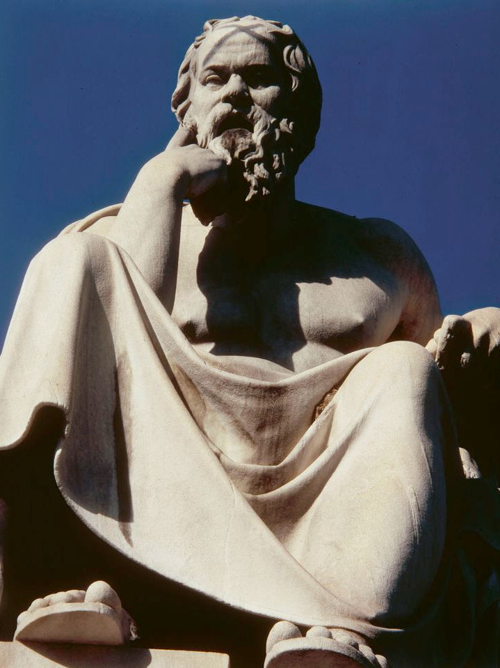 Statue av en sittende Sokrates som holder hånda opp mot ansiktet og ser betenkt ut. Foto.