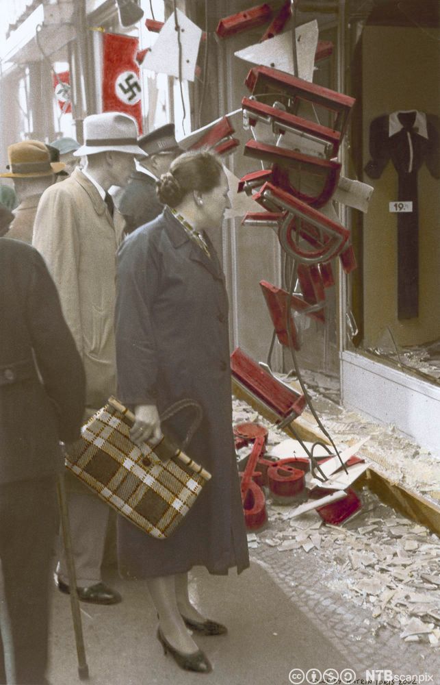 Kvinne som ser på eit øydelagt utstillingsvindauge i ein jødisk butikk. Det er rett etter krystallnatta i 1938. Foto.