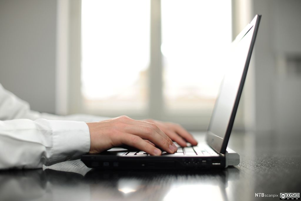 Ein person jobbar på ein berbar pc. Berre skjorteerma og hendene som tastar på tastaturet, er synlege. Foto. 
