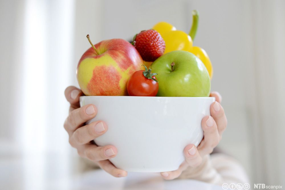 To hender held fram ein bolle med frukt, bær og grønsaker. Foto.
