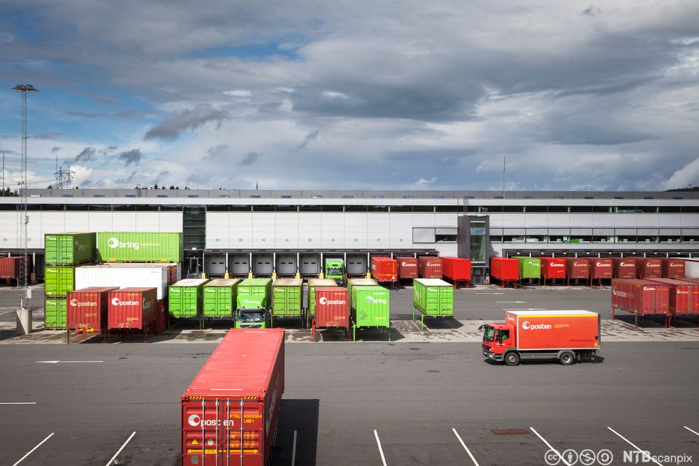Grøne og raude konteinarar står oppstilte utanfor eit stort industribygg. Foto.