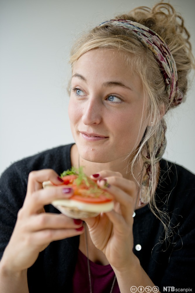 Ei ung jente spiser brødskive med hvitost og tomater. Foto.
