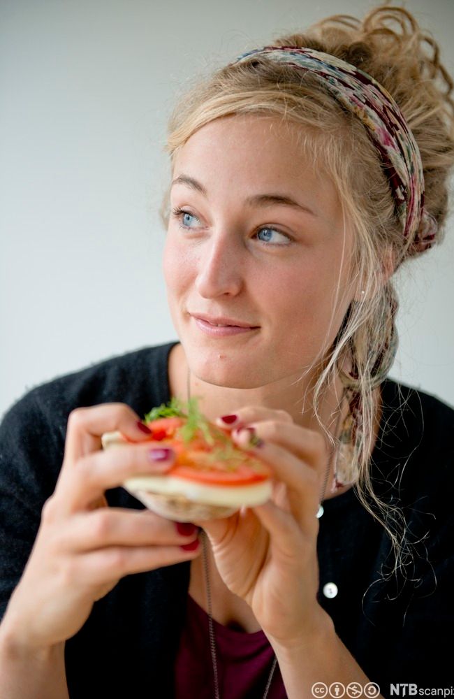 Ei ung jente spiser brødskive med hvitost og tomater. Foto.