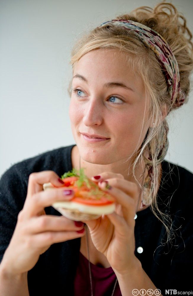 Ei ung jente et brødskive med kvitost og tomatar. Foto.