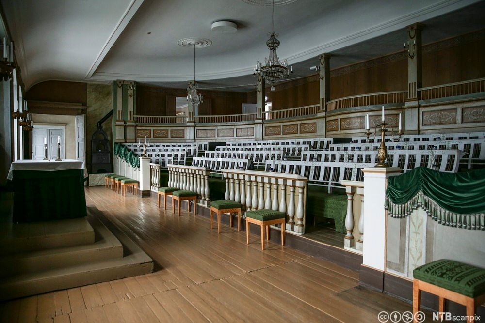 Den gamle stortingssalen slik den så ut i 1815 da den var i auditoriet på katedralskolen i Christiania. Salen har en rekke seter med grønt trekk, noen krakker står foran dem. Fremst er det et podium. Foto. 