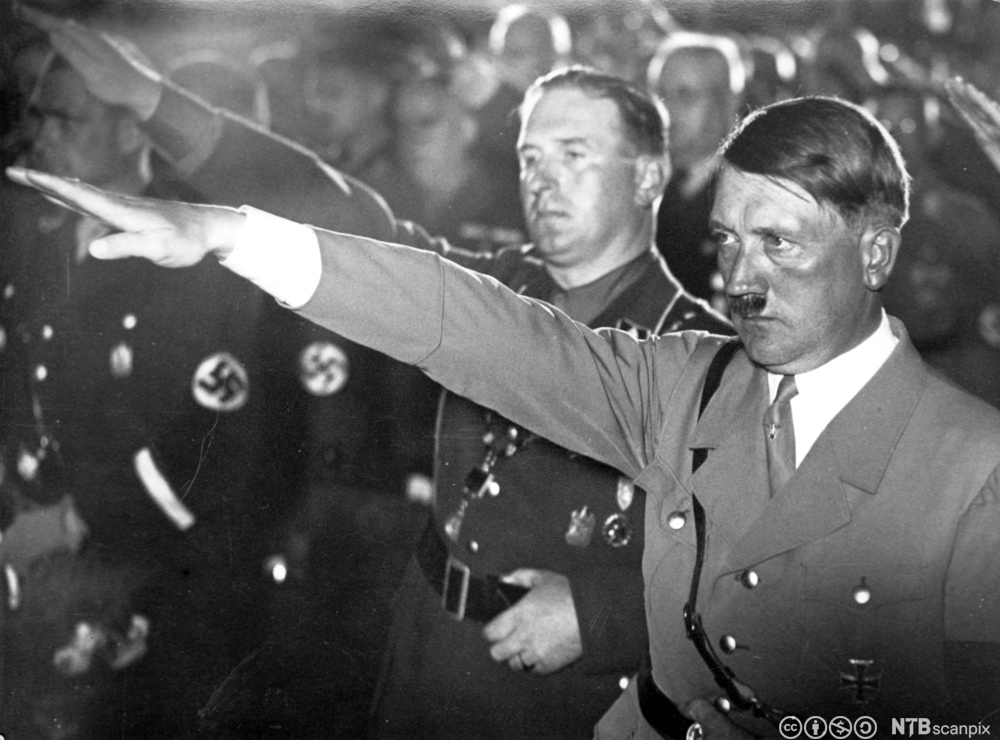 Adolf Hitler og andre menn i naziuniform gjør nazi-hilsen. Foto.