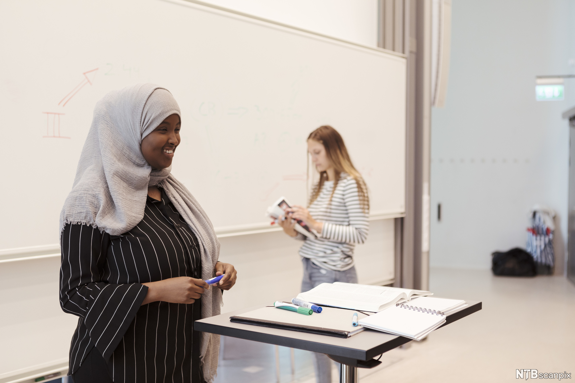 Ung, smilende kvinne presenterer foran i et klasserom. Foto.