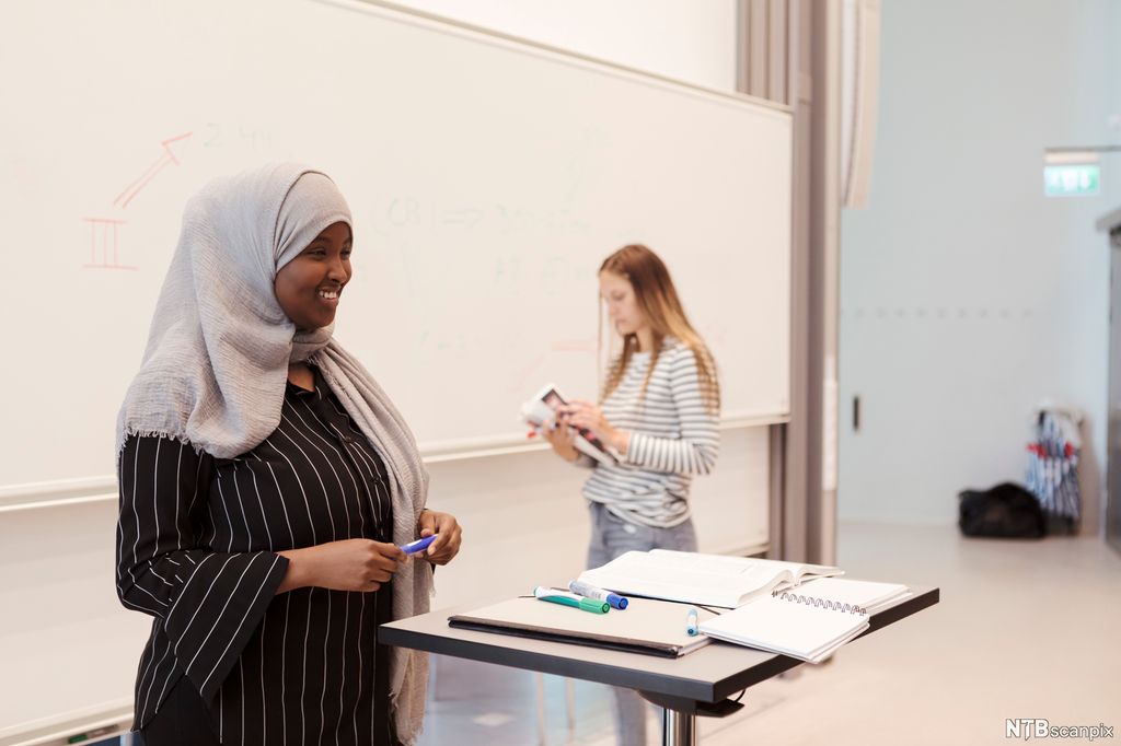 Ung mørkhudet kvinne med hidjab presenterer noe. Foto.