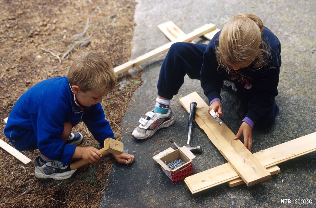 To barn som snekrer med hammer, spiker og planker. Foto.