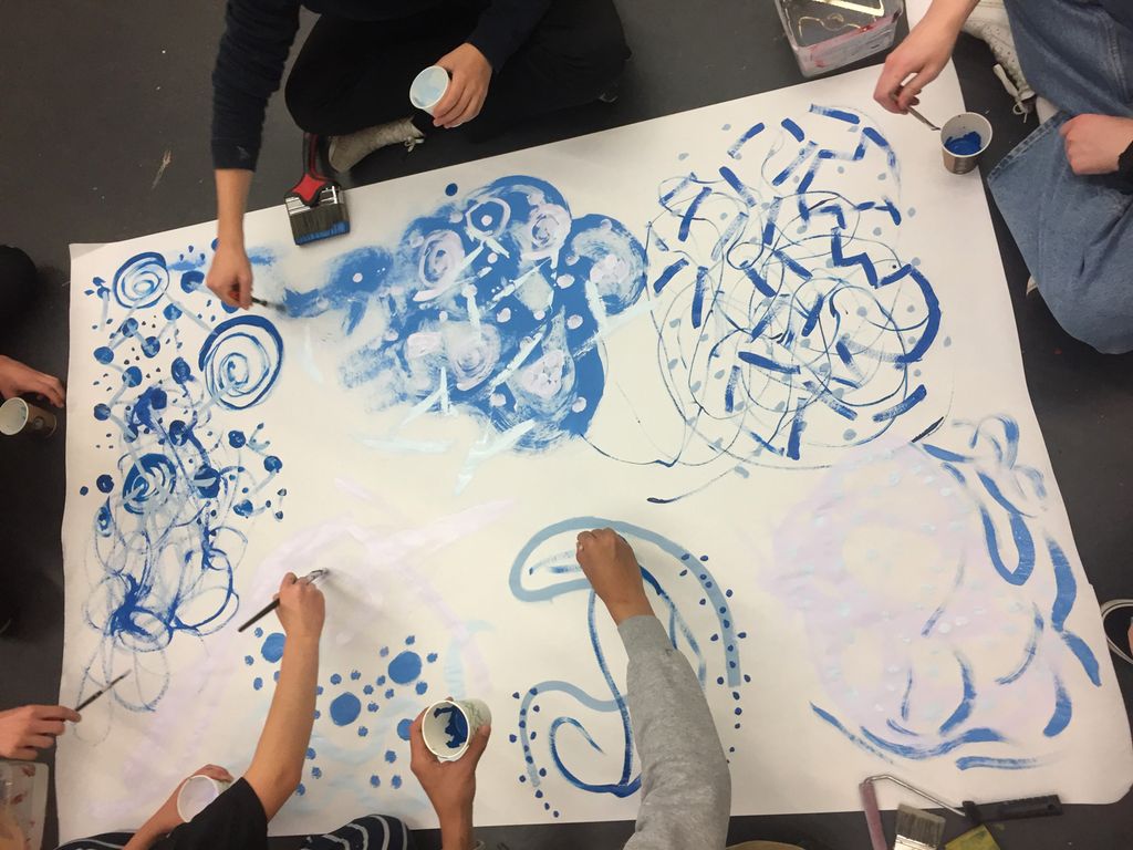 Mange hender som maler på et stort ark. Foto.