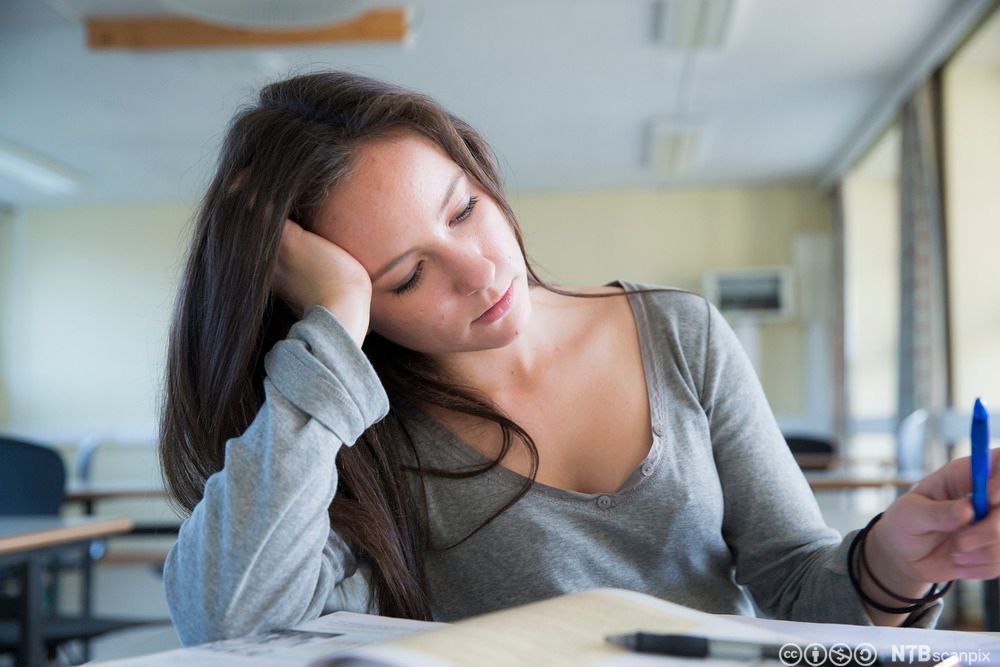 Jente sitter alene i et klasserom og leser og noterer. Foto.
