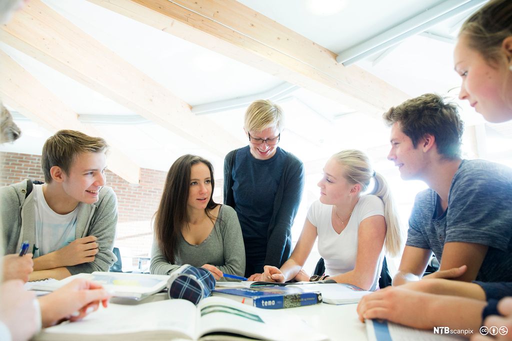 Videregående elever sitter og jobber med gruppearbeid, og læreren står ved siden av og hjelper. Foto.