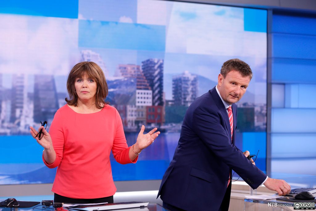 Ingvild Bryn og Jon Gelius bak disken i studioet til Dagsrevyen. Hun gestikulerer og ser i kamera, han rydder sammen myggmikrofonen sin. Foto.
