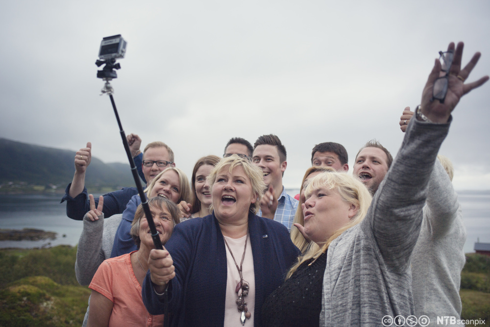 Erna Solberg holder i en selfiestang og tar selfie sammen med ei gruppe personer. Foto.