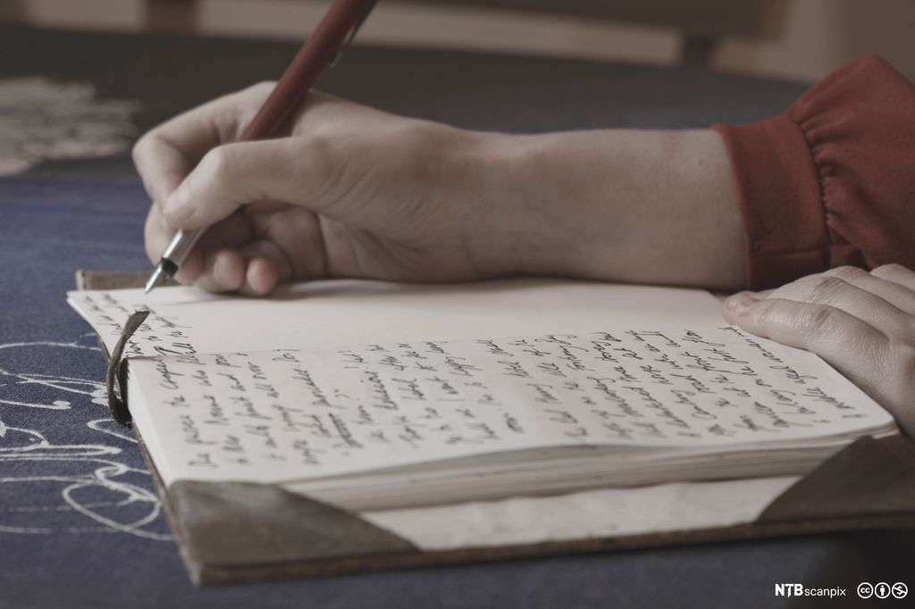 Hånd som skriver i ei bok. Foto.