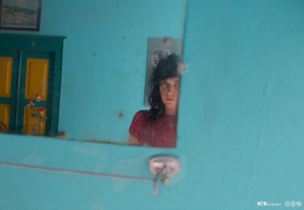 Speilbilde av ung kvinne i blått rom. Foto.