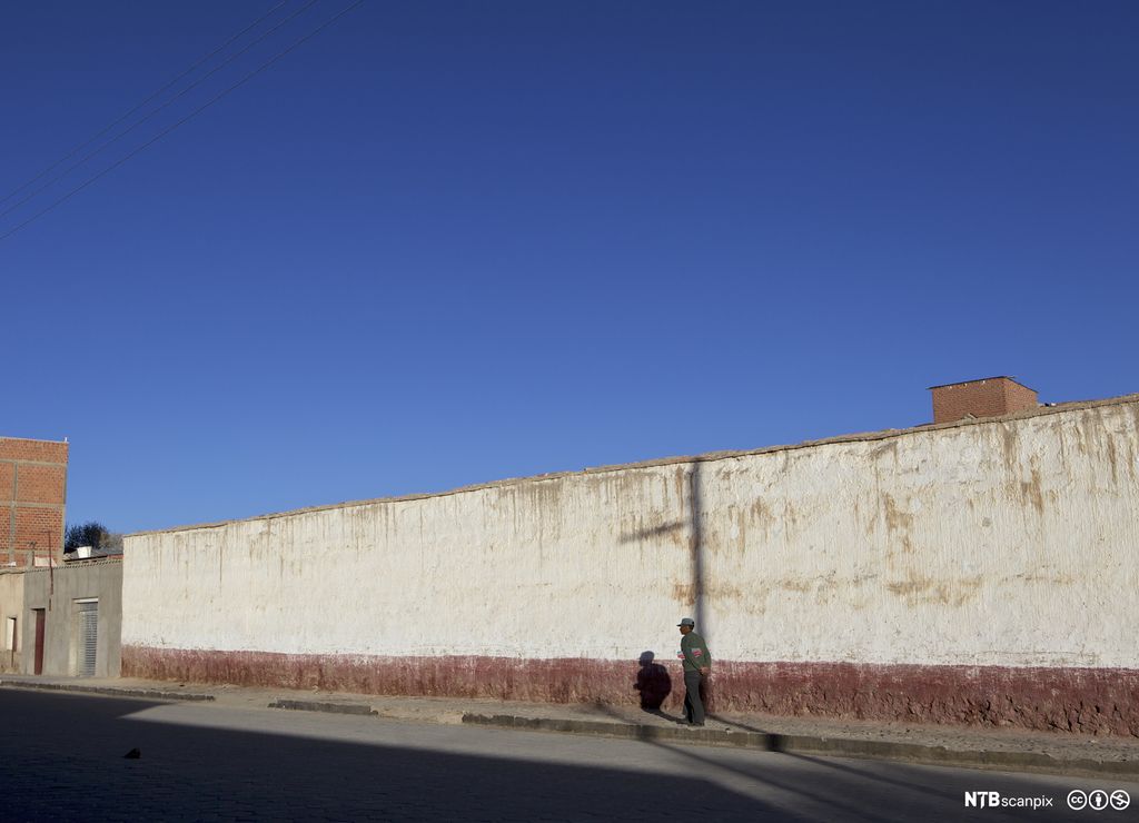 Mann går langs mur. Foto.