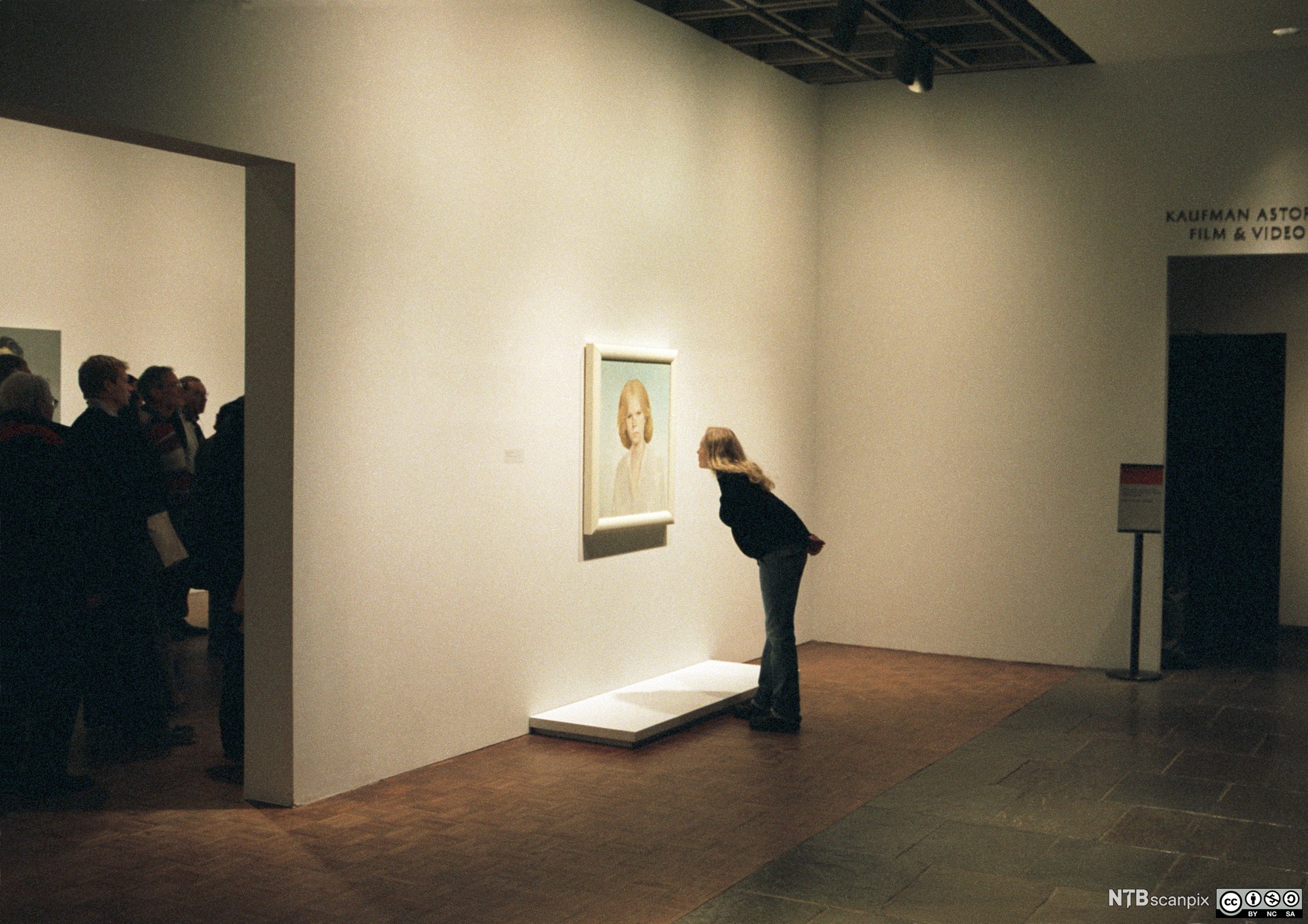 A young woman in an art museum is studying a portrait of another woman. She's bending forwards, studying the details of the painting. Photo. 