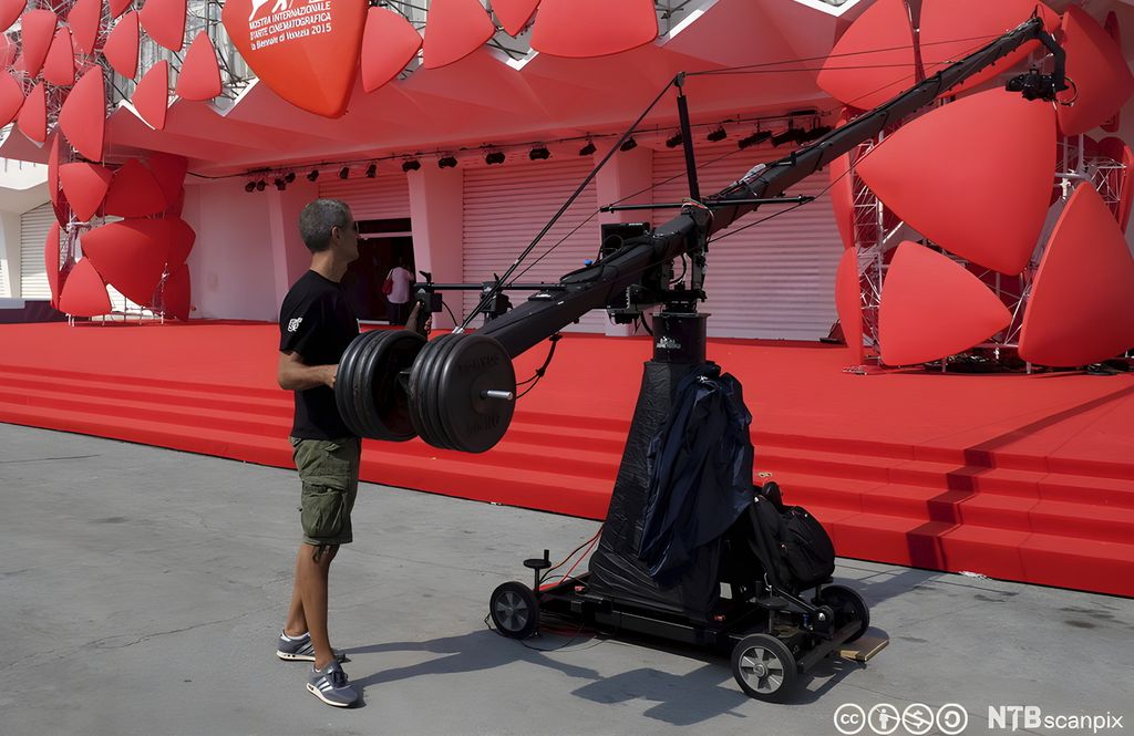 Ein mann tiltar eit kamera ved hjelp av ei kran. Foto.