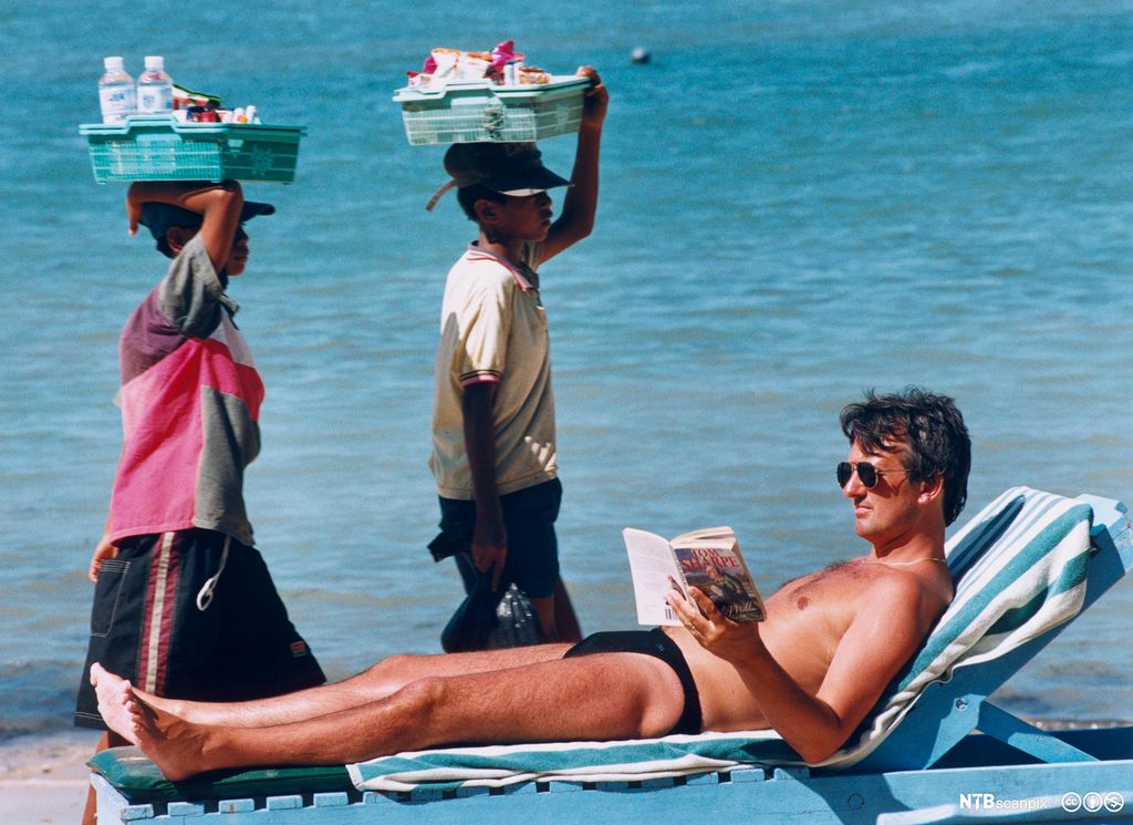 Turist på solseng slapper av på stranda. Foto.