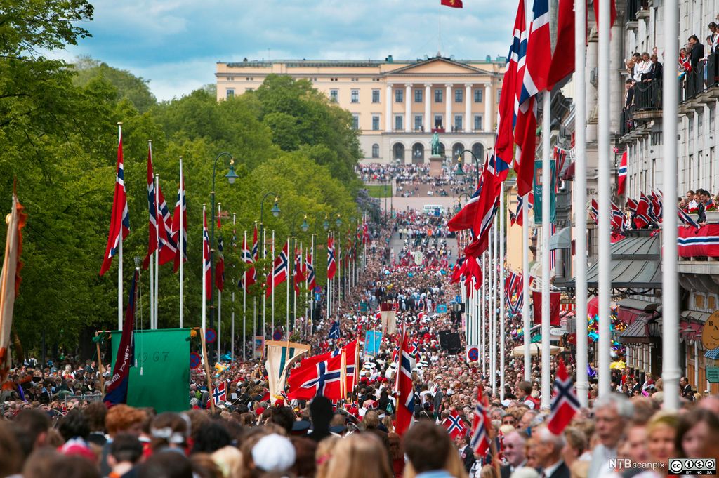 17. mai på Karl Johans gate i Oslo. Slottet ligger på høyden i enden av gata der det vrimler av folk og norske flagg. Foto.