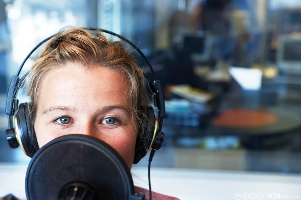 Kvinne som snakkar i mikrofon i radiostudio. Foto.