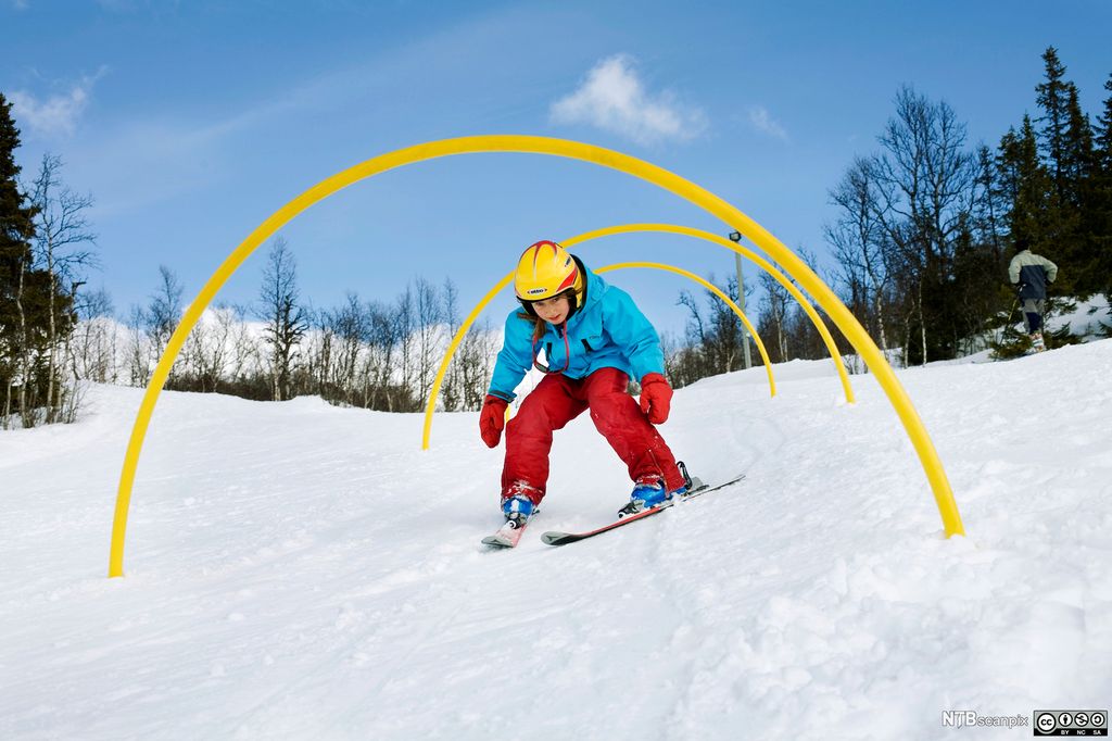 Et barn på ski som kryper gjennom bøyle. Foto.