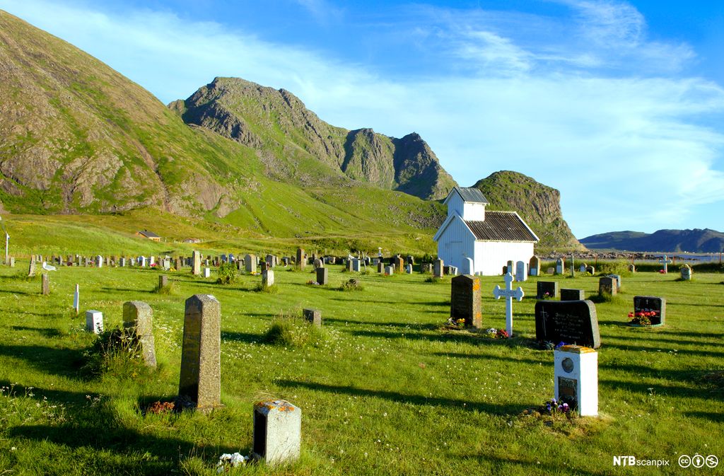 Liten hvit kirke omgitt av gravstøtter. Foto.