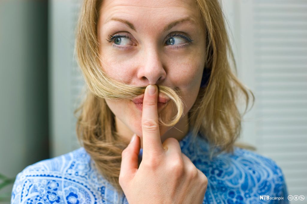 Kvinne som ser tankefull ut og holder en hårlokk under nesa. Foto.