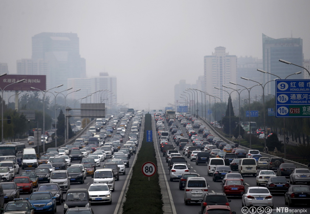Tett trafikk av bilar i åtte køyrebanar med eit lokk av forureina luft over Beijing. Foto.