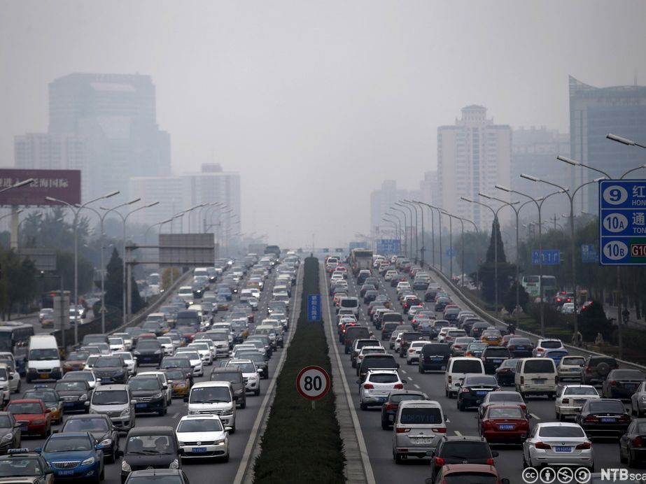 Tett trafikk av bilar i åtte køyrebanar med eit lokk av forureina luft over Beijing. Foto.