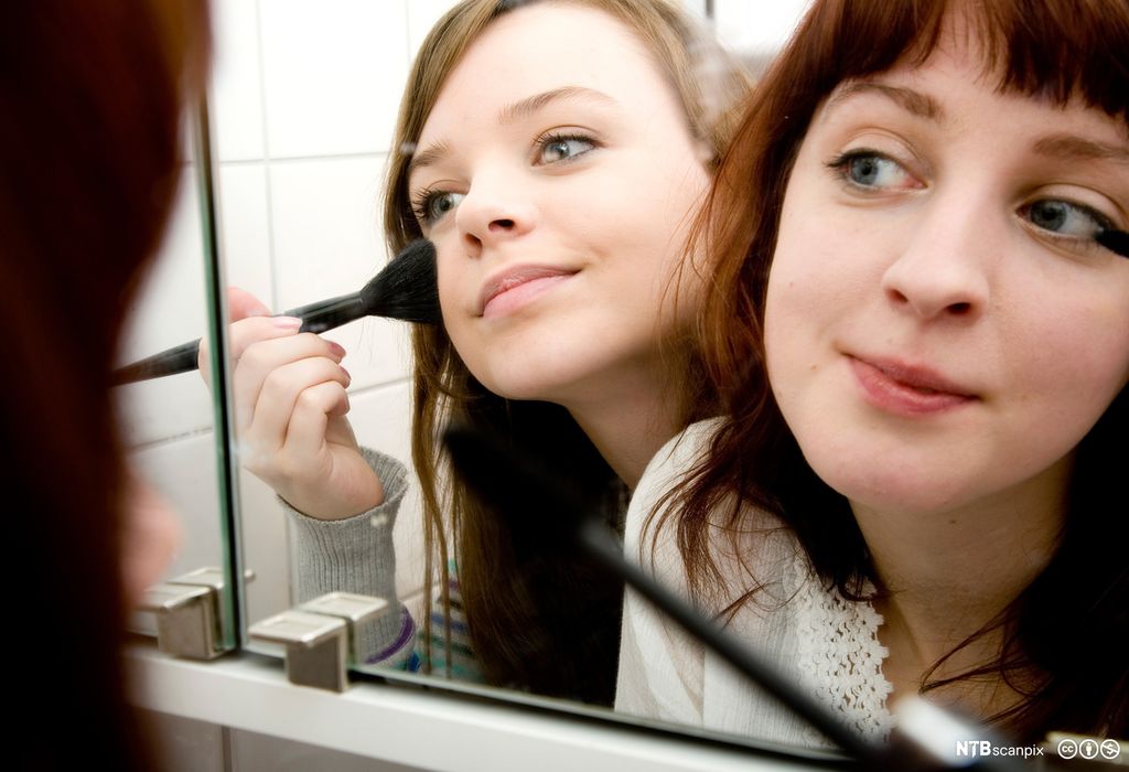 To jenter sminker seg foran et speil. Foto.